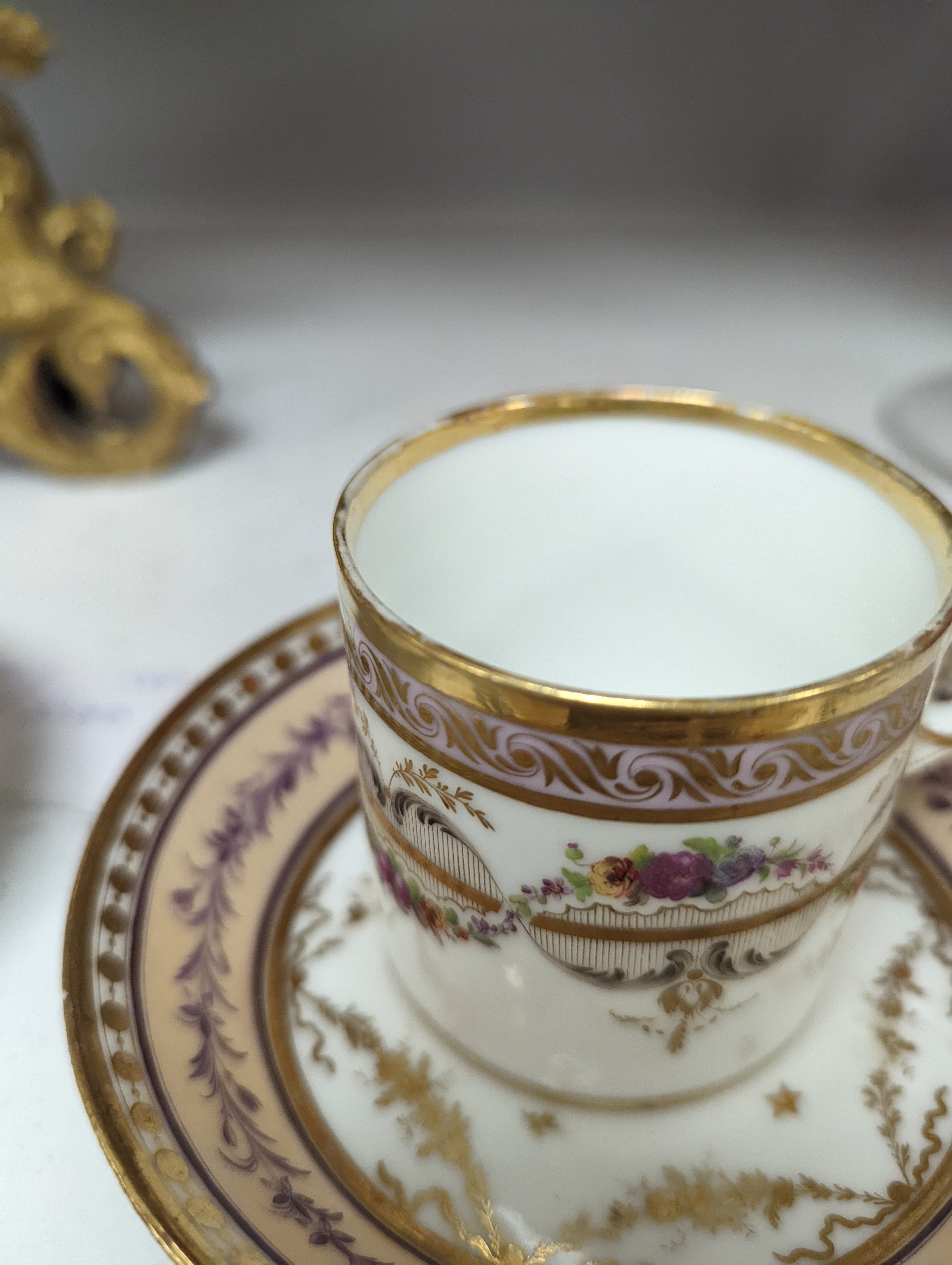 A Duc d'Angouleme coffee can and saucer painted with a puce chain of leaves on a salmon coloured ground and another painted with a flower chain, black feather and a gilt line, latter with stencilled red mark 'Manuf de M